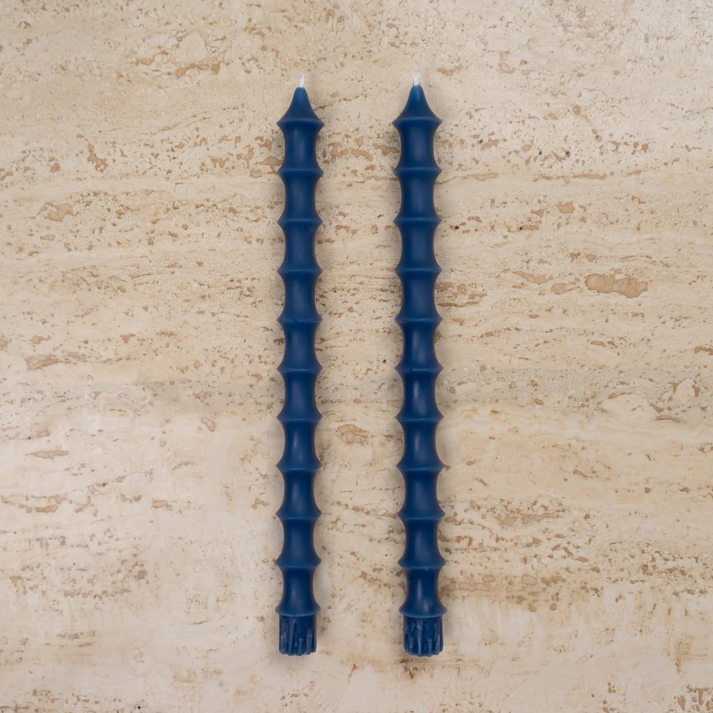 Hand-poured bamboo pagoda beeswax taper candles in lucid blue color, set of two on travertine surface