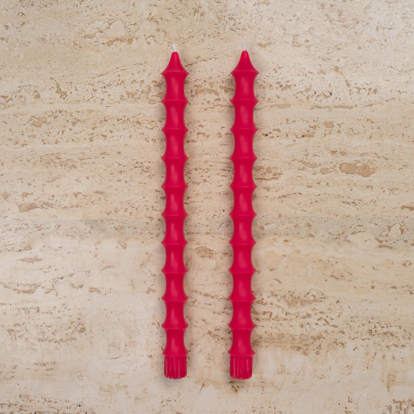 Hand-poured bamboo pagoda beeswax taper candles in dragonfruit pink color, set of two on travertine surface