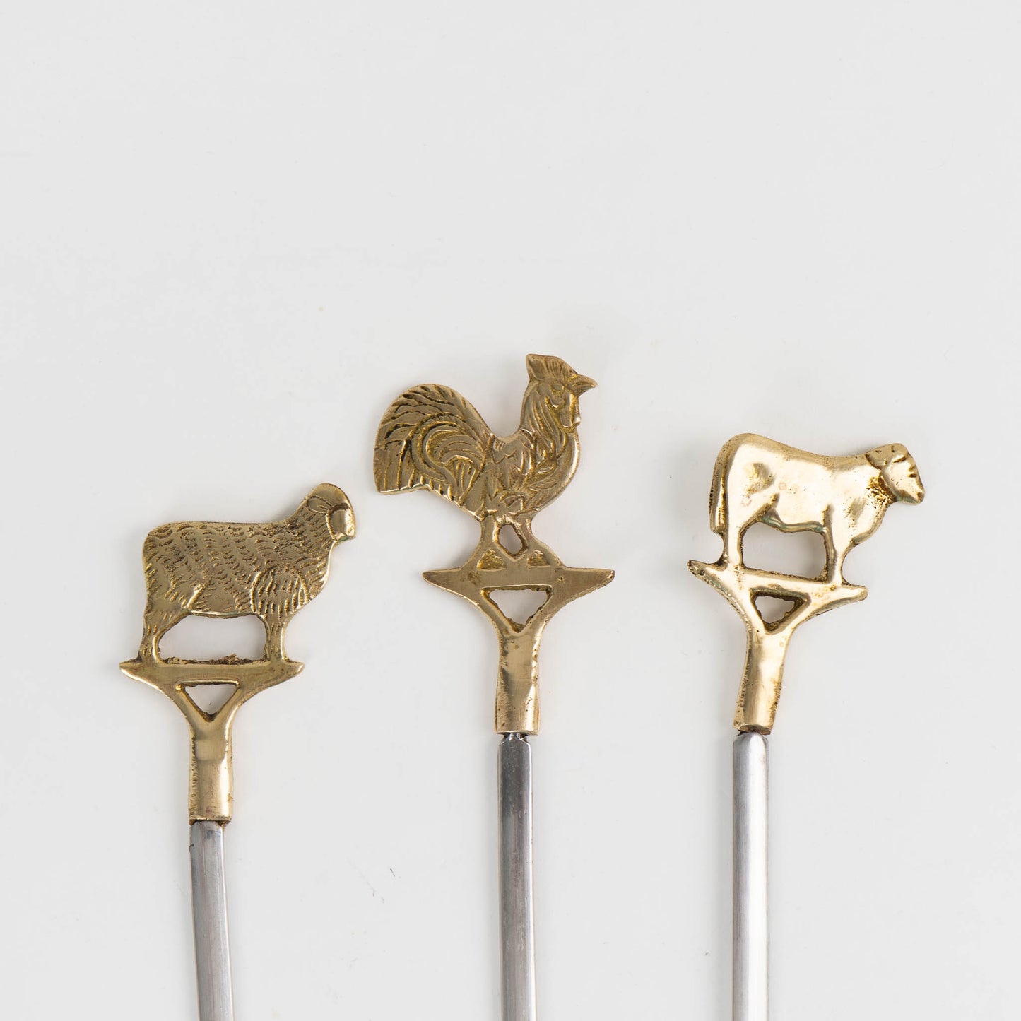 Close up of vintage brass animal barbecue skewers with stainless steel blades, featuring sheep, rooster, cow, handles from the 1960s-70s