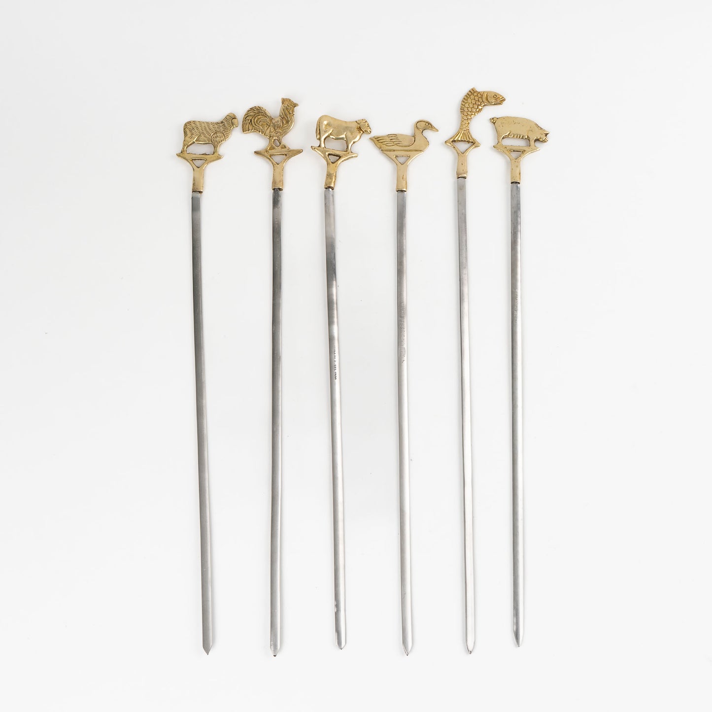 Set of six vintage brass animal barbecue skewers with stainless steel blades, featuring sheep, rooster, cow, duck, fish, and pig handles from the 1960s-70s