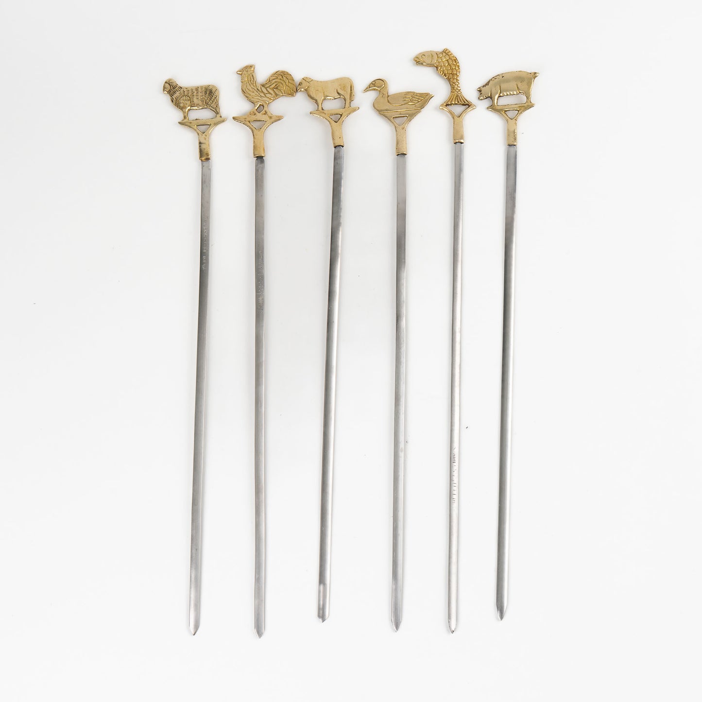 Set of six vintage brass animal barbecue skewers with stainless steel blades, featuring sheep, rooster, cow, duck, fish, and pig handles from the 1960s-70s