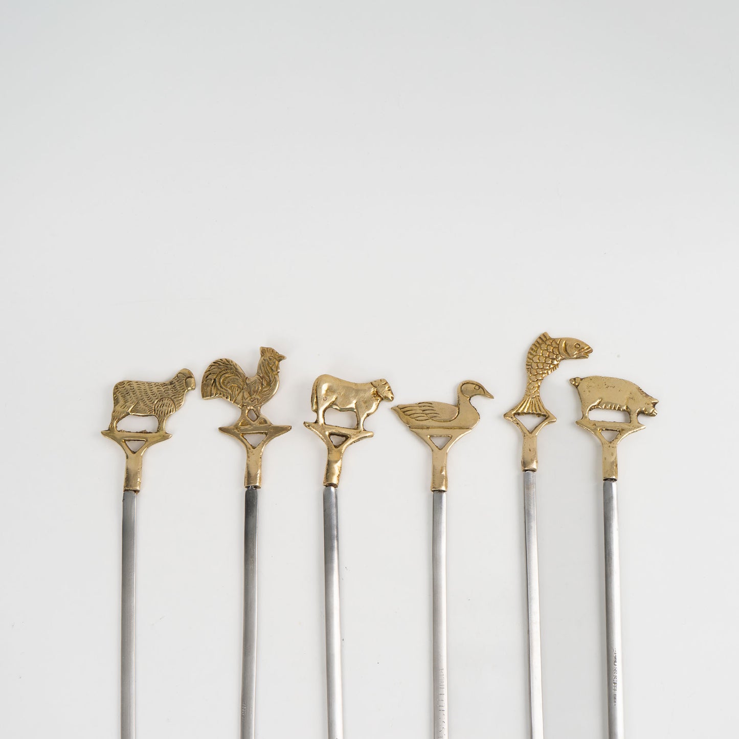 close up of Set of six vintage brass animal barbecue skewers with stainless steel blades, featuring sheep, rooster, cow, duck, fish, and pig handles from the 1960s-70s