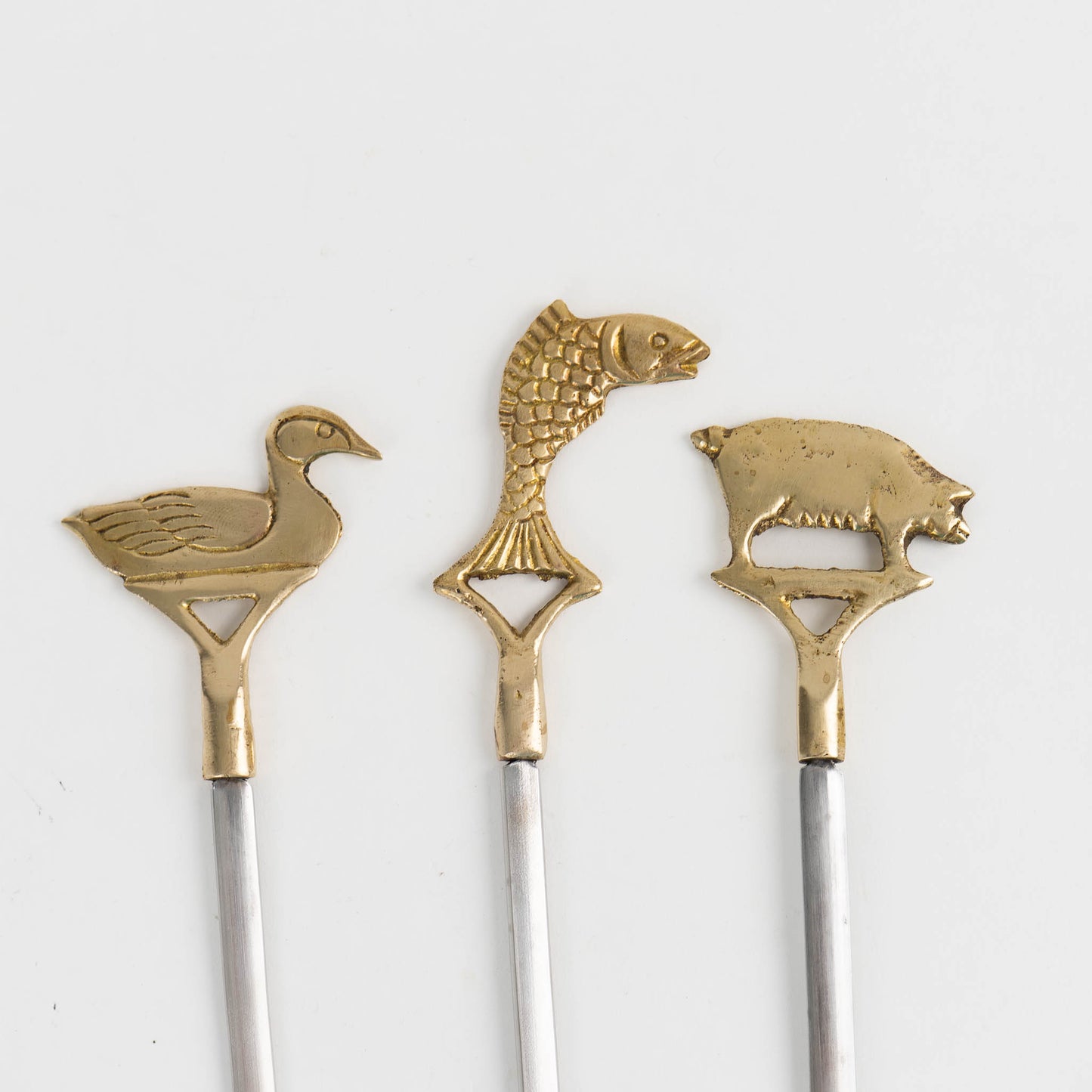 Close up of  vintage brass animal barbecue skewers with stainless steel blades, featuringduck, fish, and pig handles from the 1960s-70s 