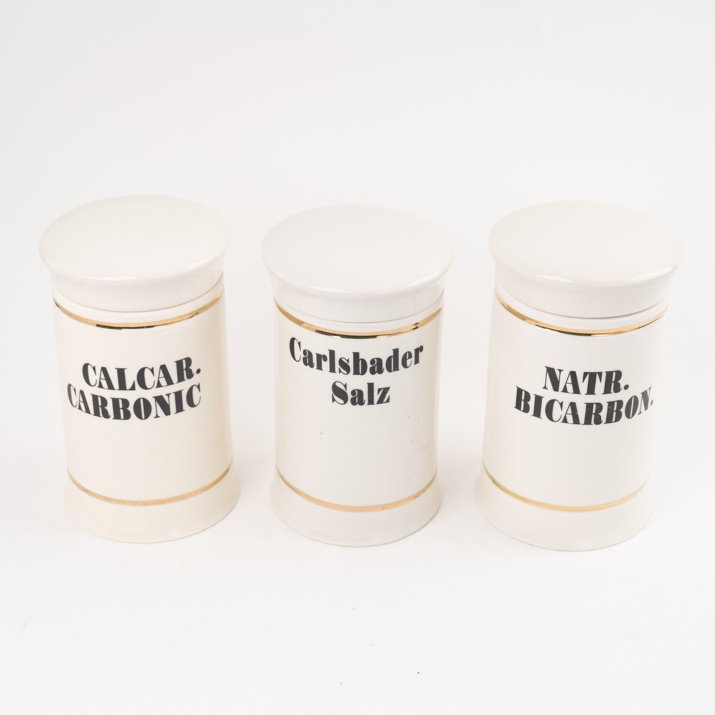 Set of three off-white ceramic apothecary jars with gold stripes and black vintage lettering with matching lids 