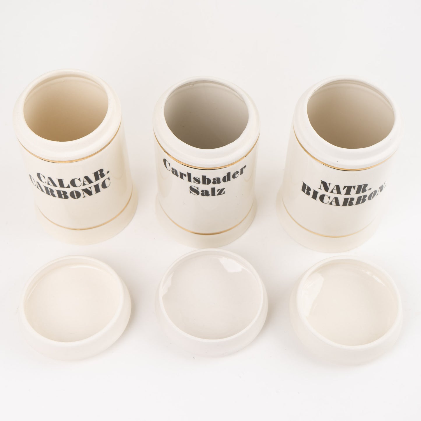 Set of three off-white ceramic apothecary jars with gold stripes and black vintage lettering with matching lids 
