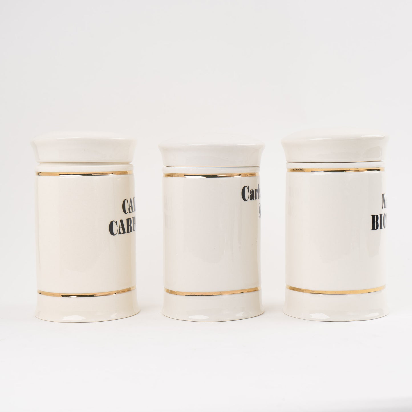Set of three off-white ceramic apothecary jars with gold stripes and black vintage lettering with matching lids 