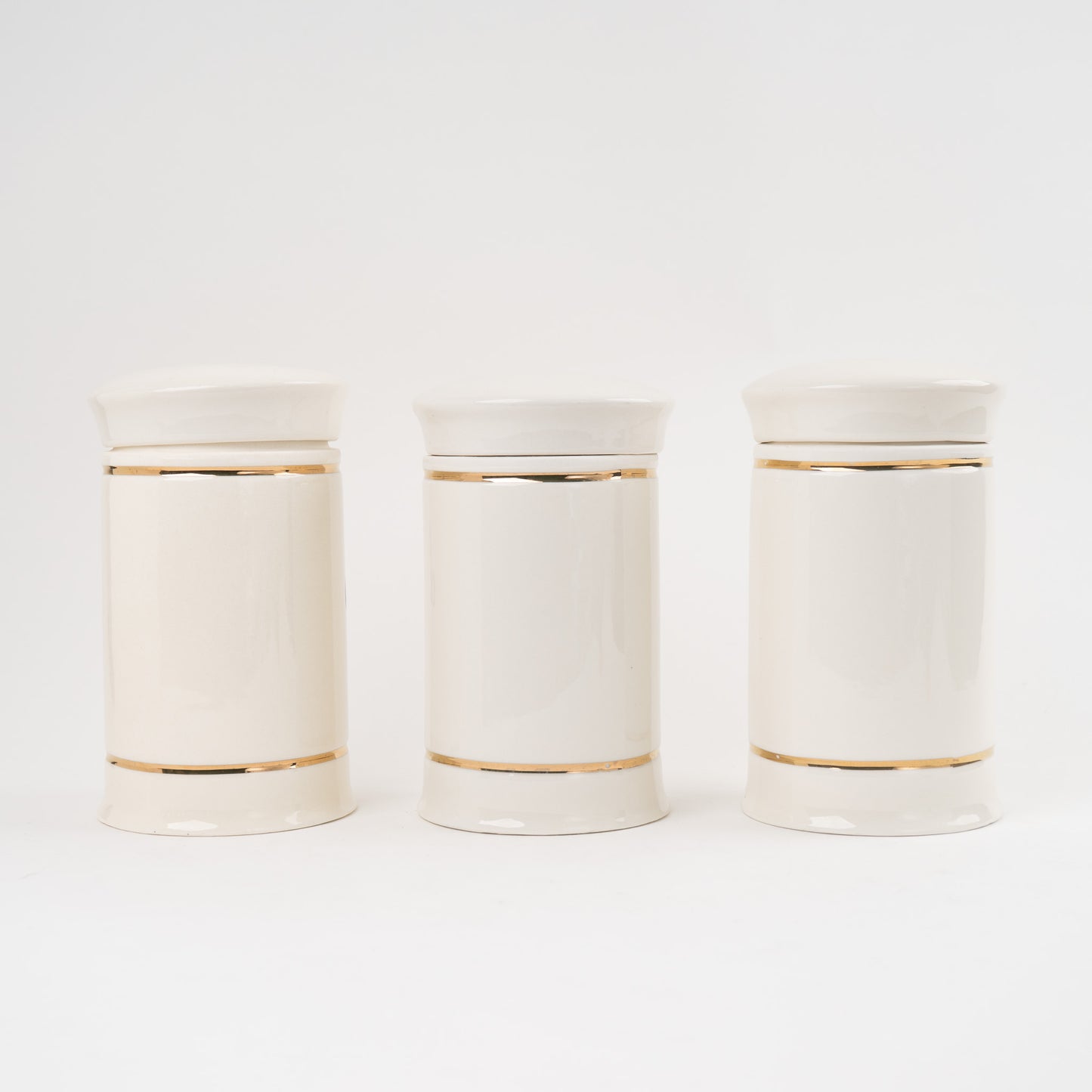 Set of three off-white ceramic apothecary jars with gold stripes and black vintage lettering with matching lids 
