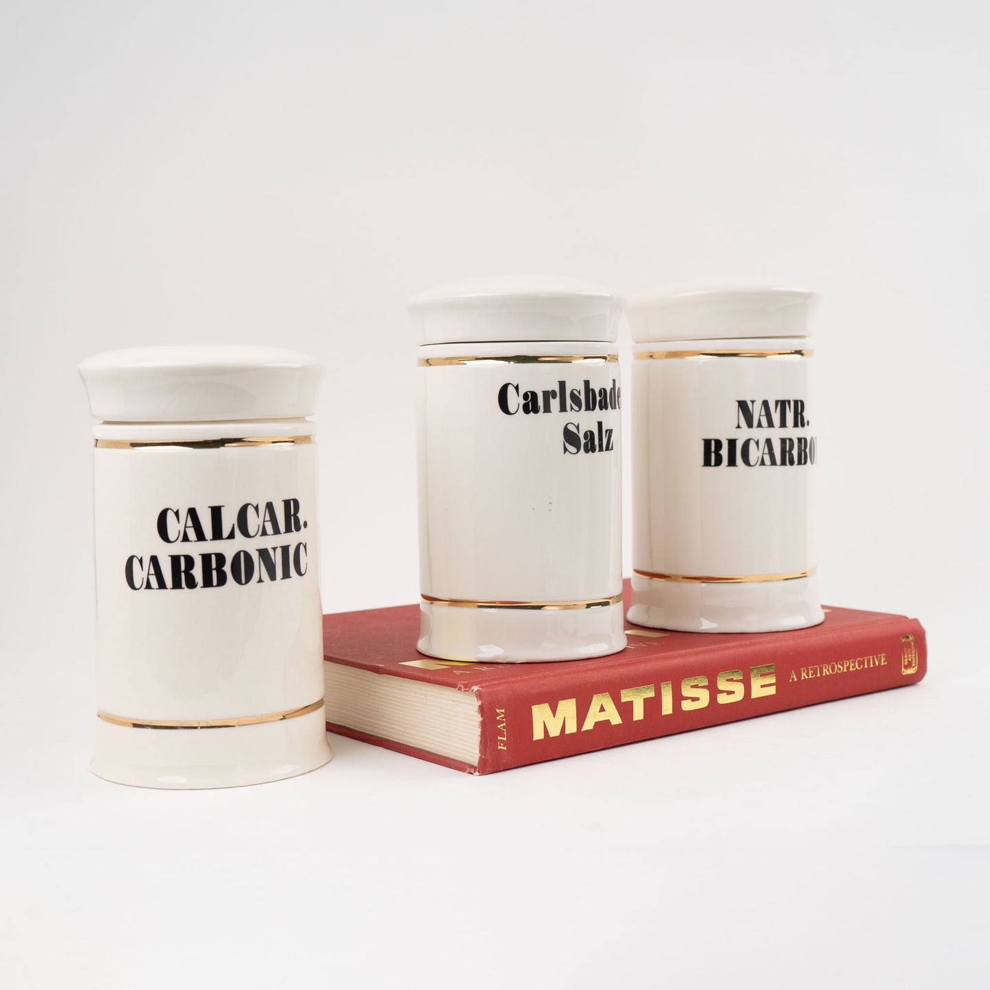 Set of three off-white ceramic apothecary jars with gold stripes and black vintage lettering with matching lids 