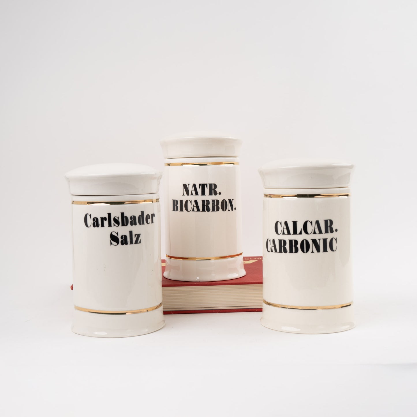 Set of three off-white ceramic apothecary jars with gold stripes and black vintage lettering with matching lids 