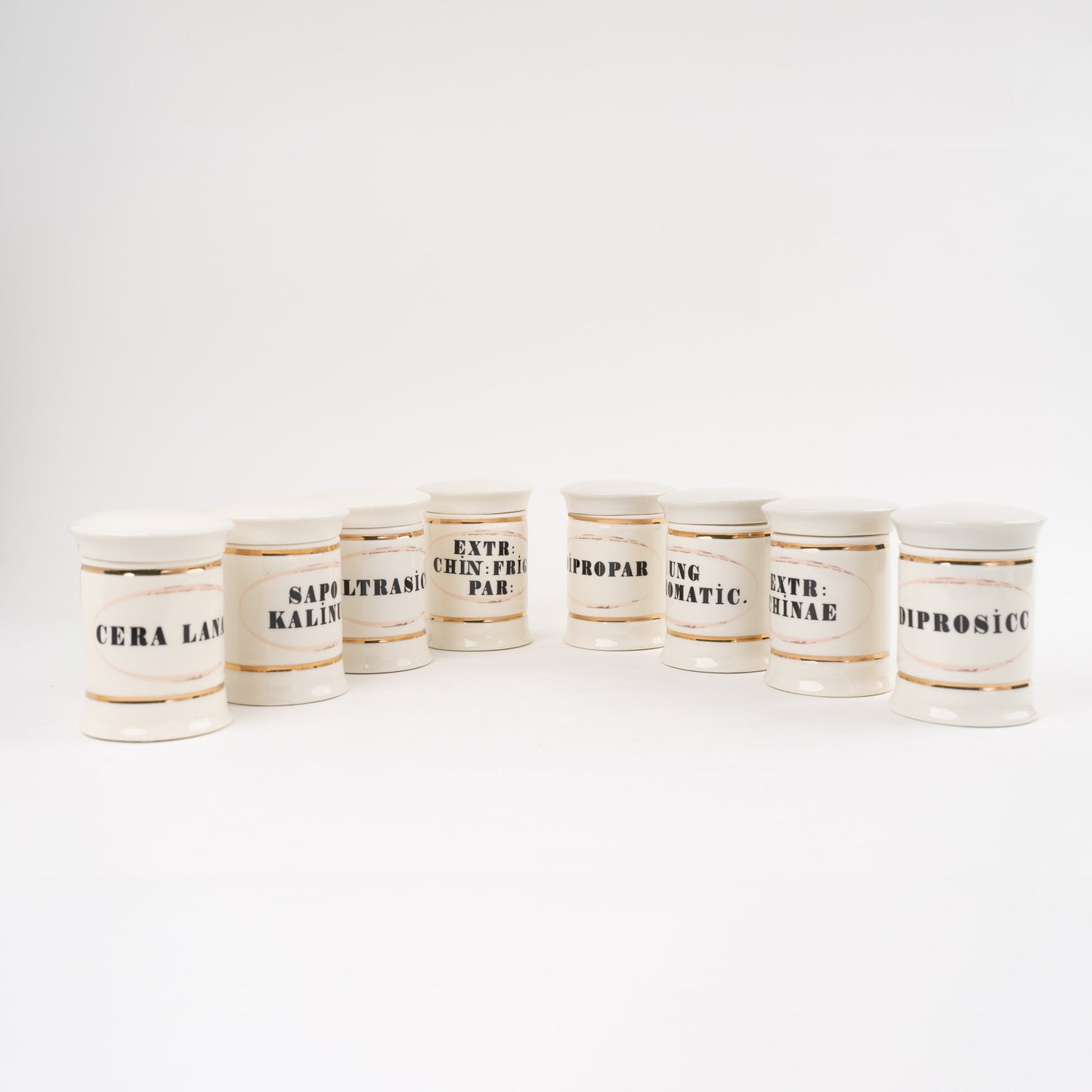 Set of 8 off-white ceramic apothecary jars with gold accents and vintage pharmaceutical-style lettering, each with matching lid