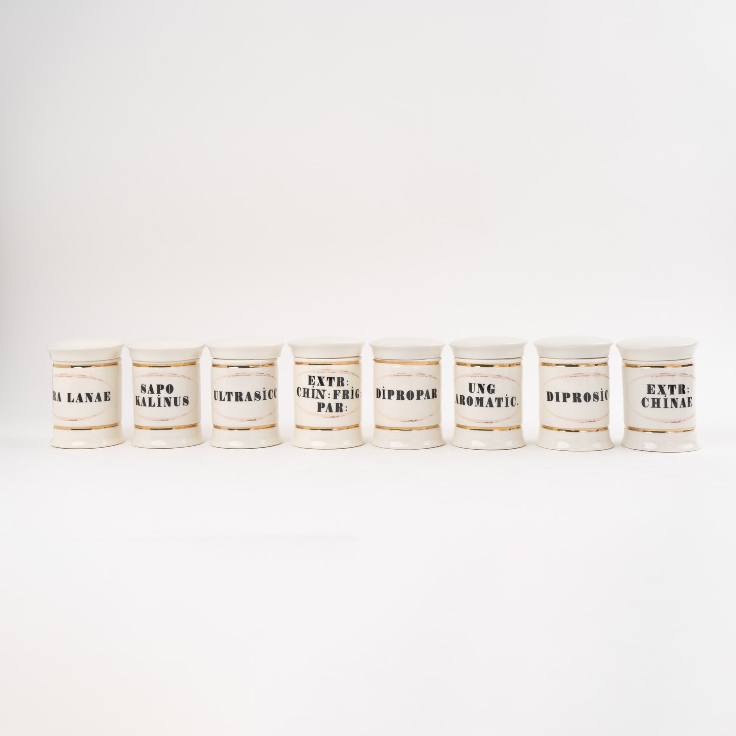 Set of 8 off-white ceramic apothecary jars with gold accents and vintage pharmaceutical-style lettering, each with matching lid