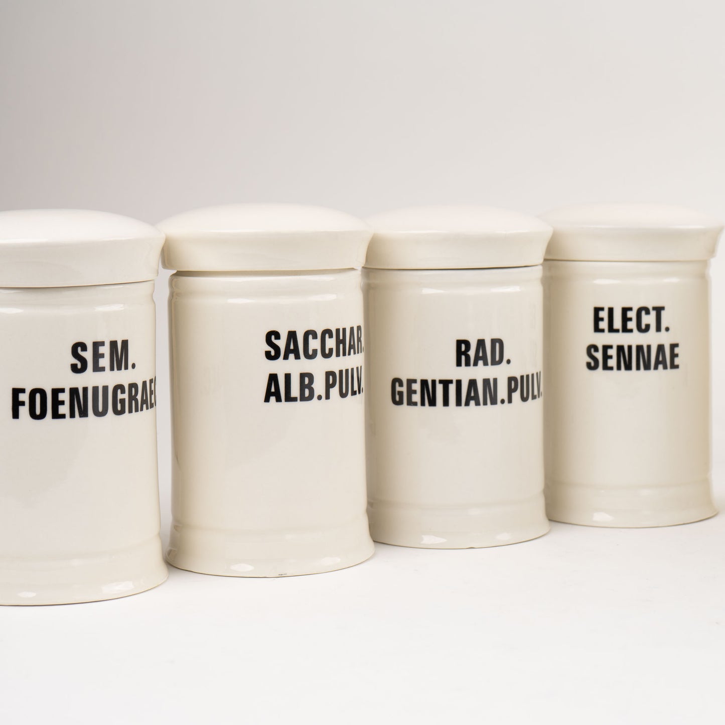 Off-white ceramic apothecary jars with black vintage lettering and matching lids 