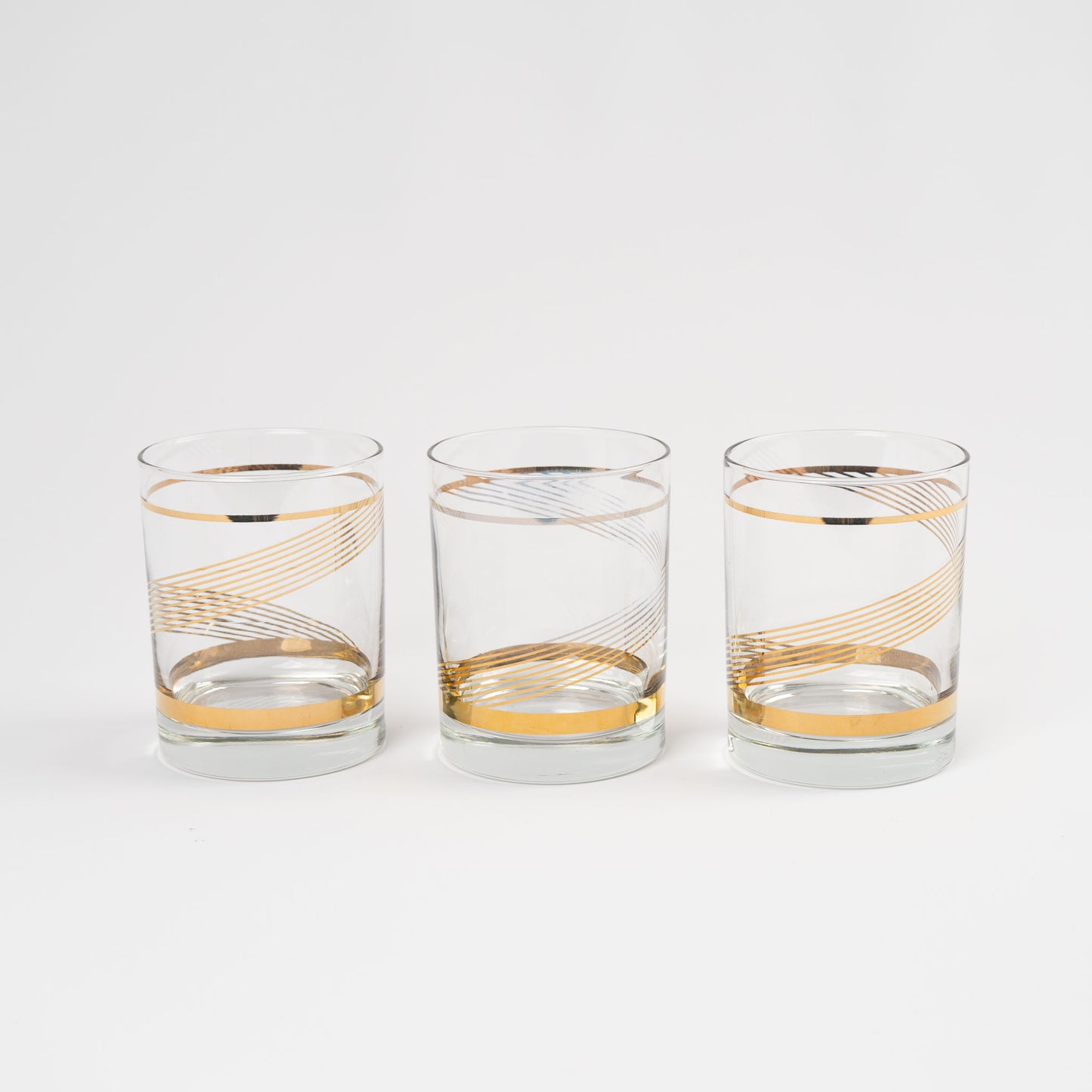 Three vintage lowball cocktail glasses with gold swirl band pattern on clear glass