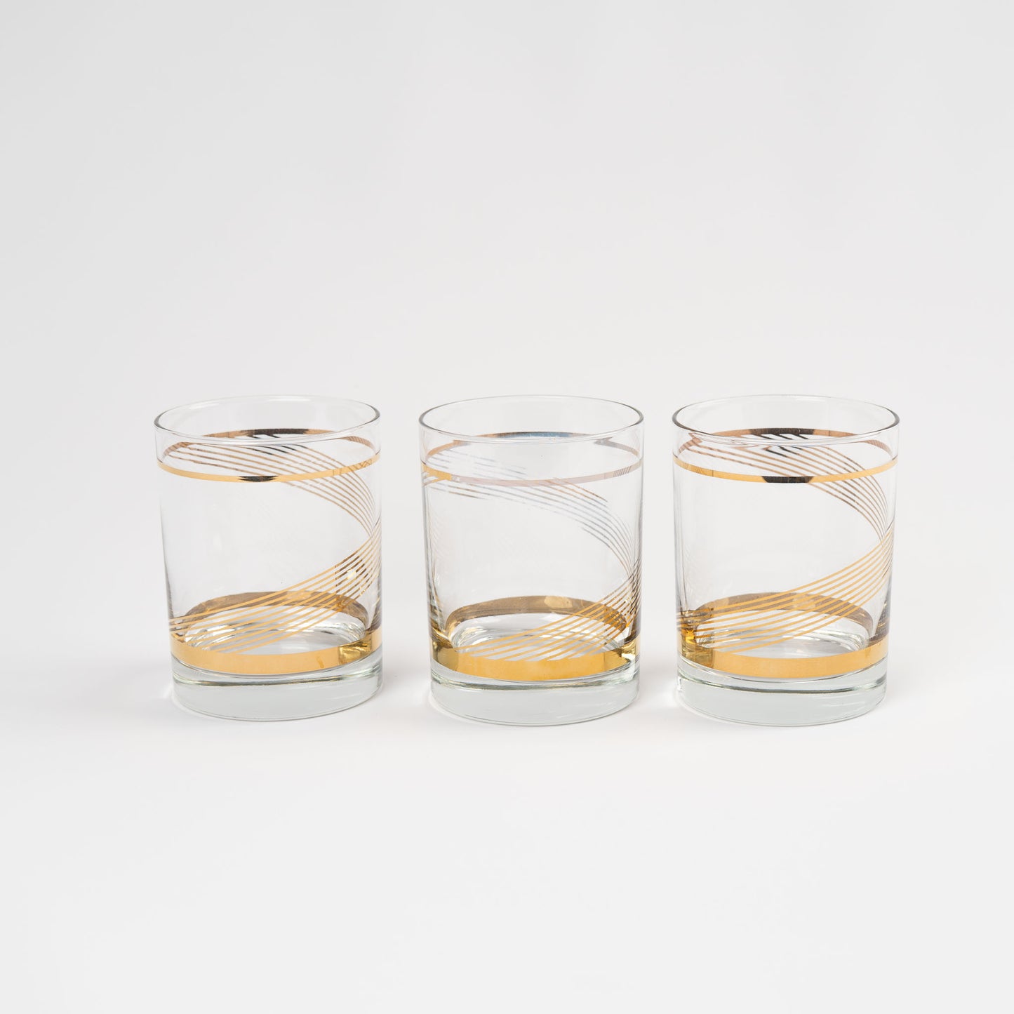 Three vintage lowball cocktail glasses with gold swirl band pattern on clear glass