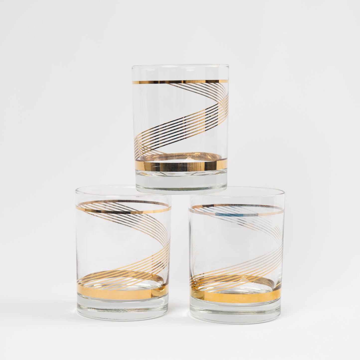 Three vintage lowball cocktail glasses with gold swirl band pattern on clear glass