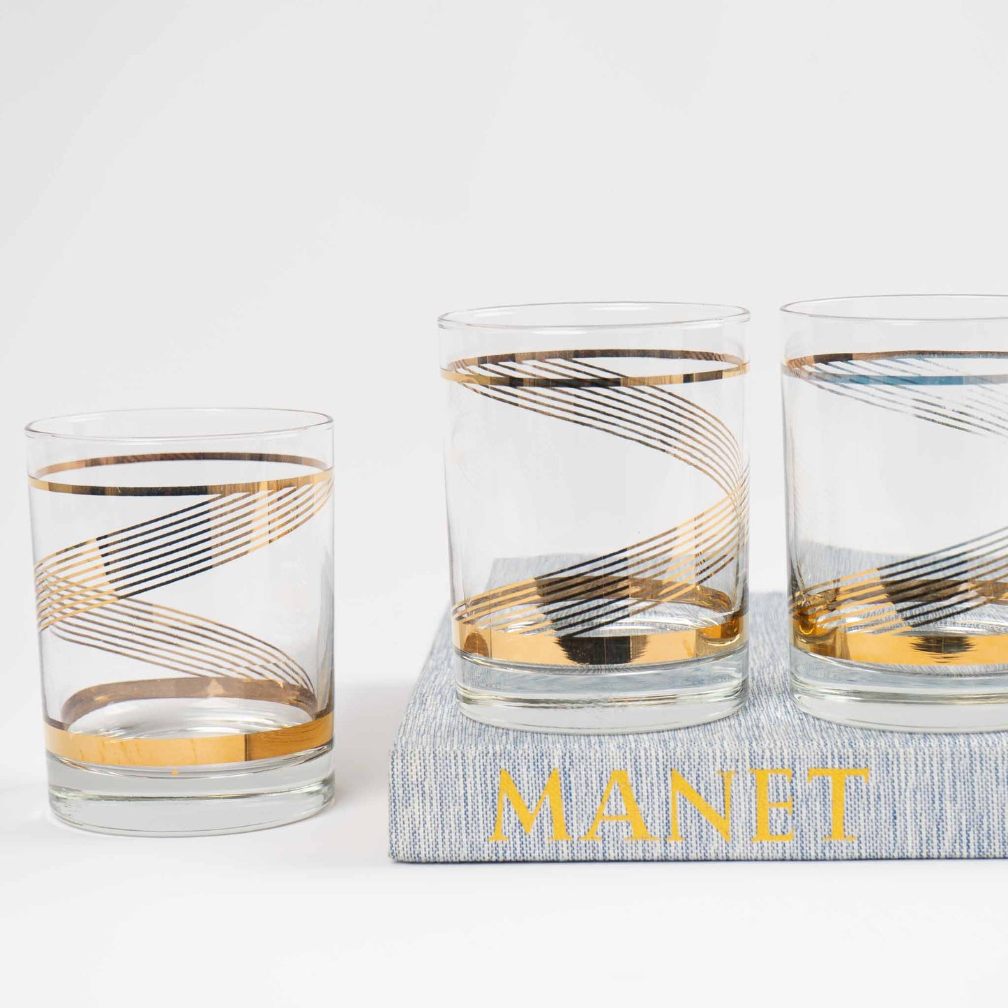 Three vintage lowball cocktail glasses with gold swirl band pattern on clear glass