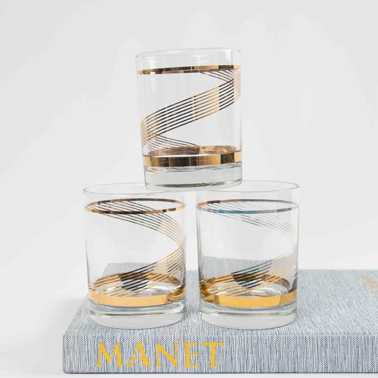 Three vintage lowball cocktail glasses with gold swirl band pattern on clear glass