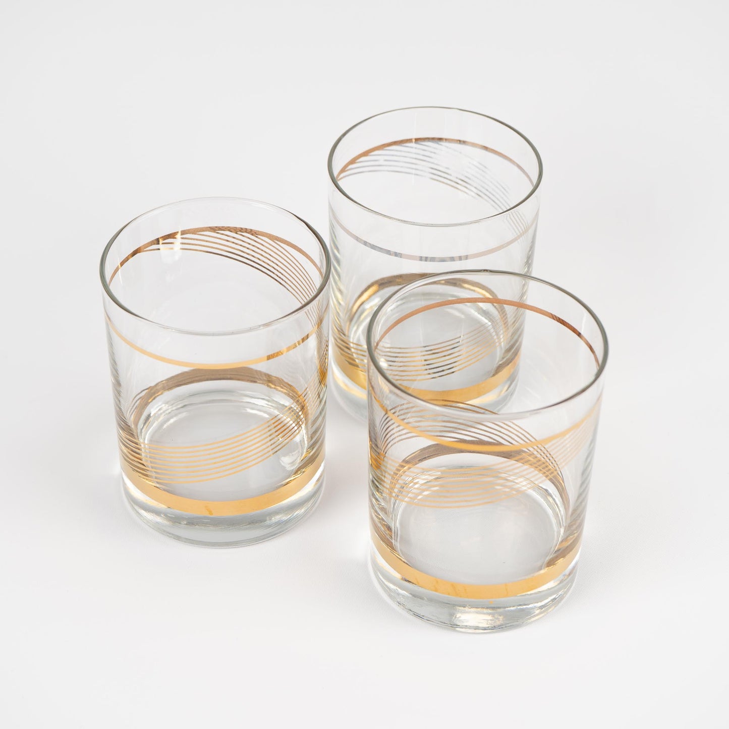 Three vintage lowball cocktail glasses with gold swirl band pattern on clear glass