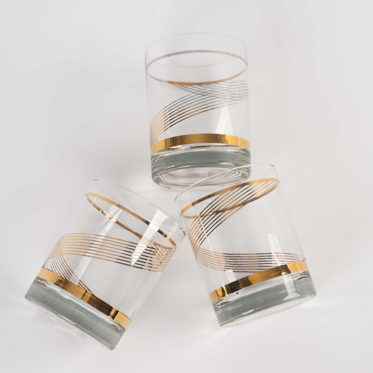 Three vintage lowball cocktail glasses with gold swirl band pattern on clear glass
