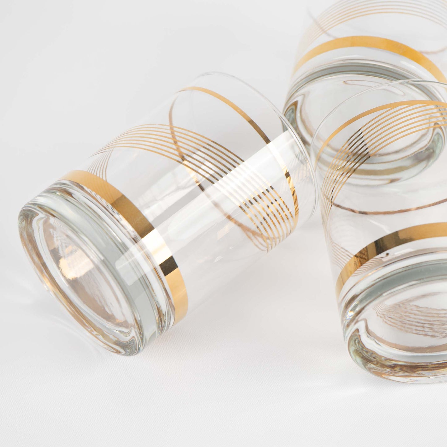 Three vintage lowball cocktail glasses with gold swirl band pattern on clear glass