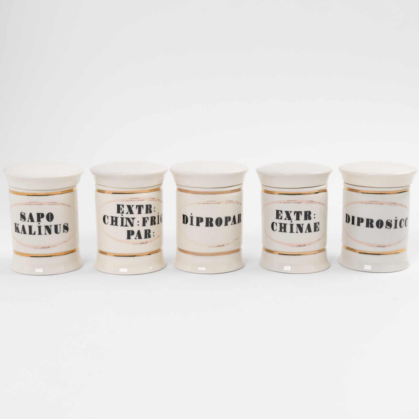 Set of 5 off-white ceramic apothecary jars with gold accents and vintage pharmaceutical-style lettering, each with matching lid