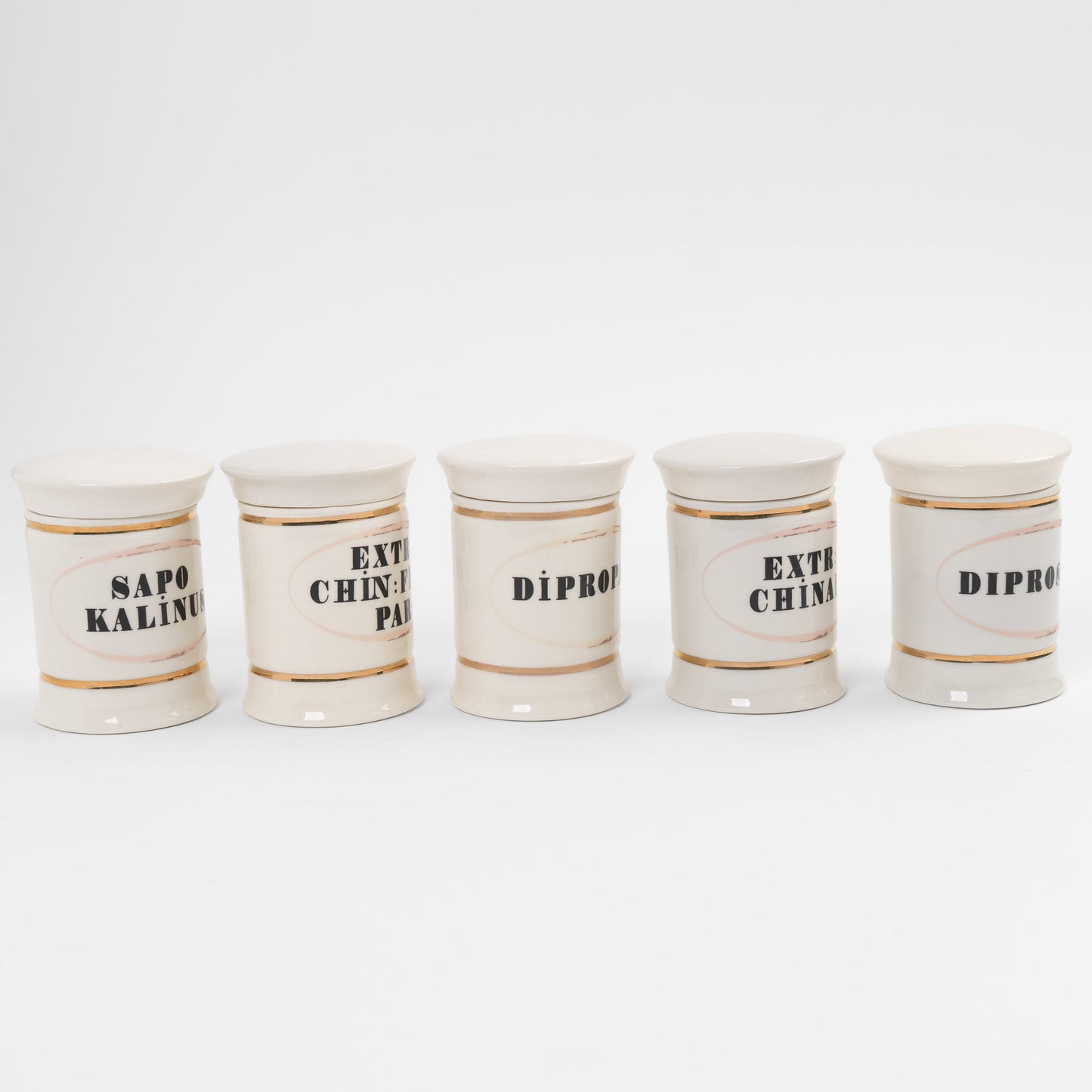 Set of 5 off-white ceramic apothecary jars with gold accents and vintage pharmaceutical-style lettering, each with matching lid