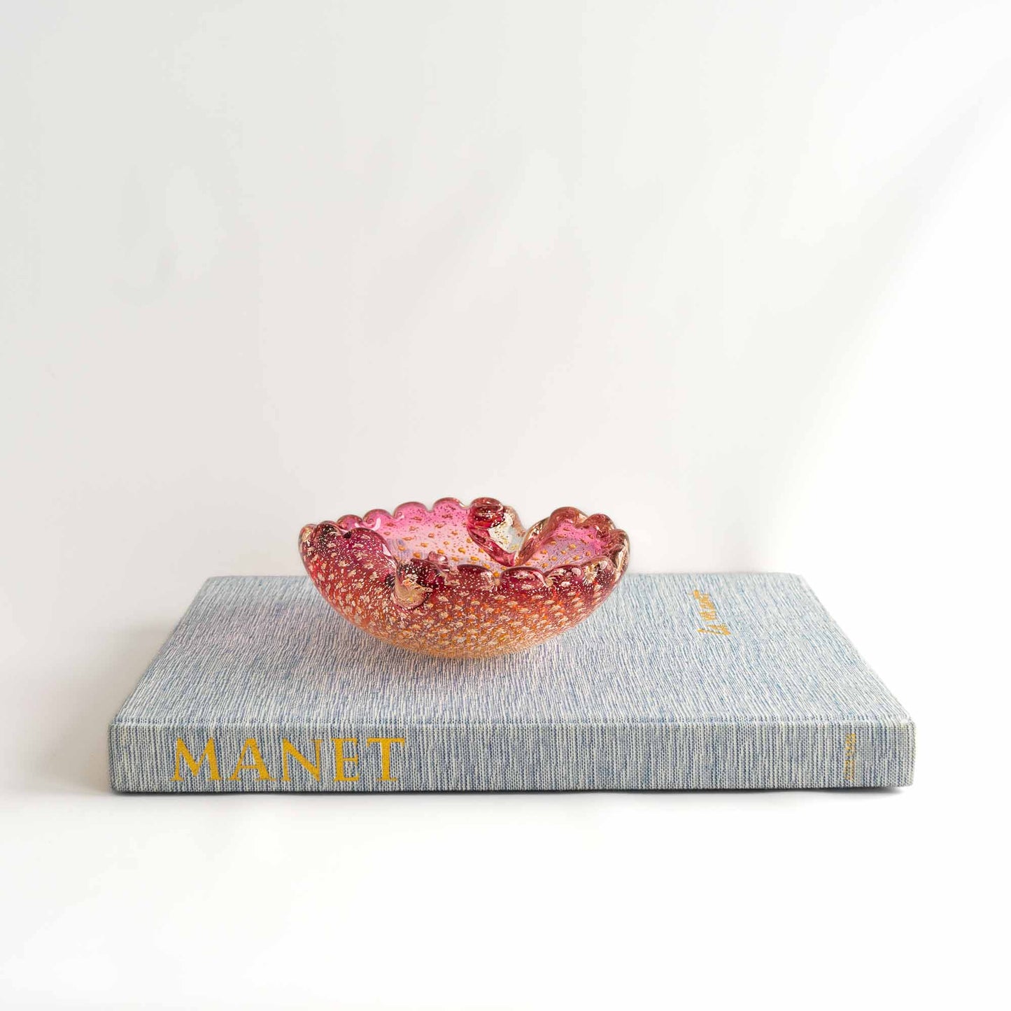 Vintage Murano Bullicante art glass catchall dish in pink and yellow with gold aventurine flecks and scalloped edge, styled on top of vintage books