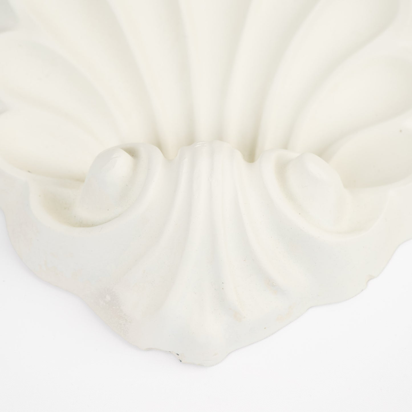 Close-up of a vintage white plaster wall shelf with ornate shell and scroll corbel detailing