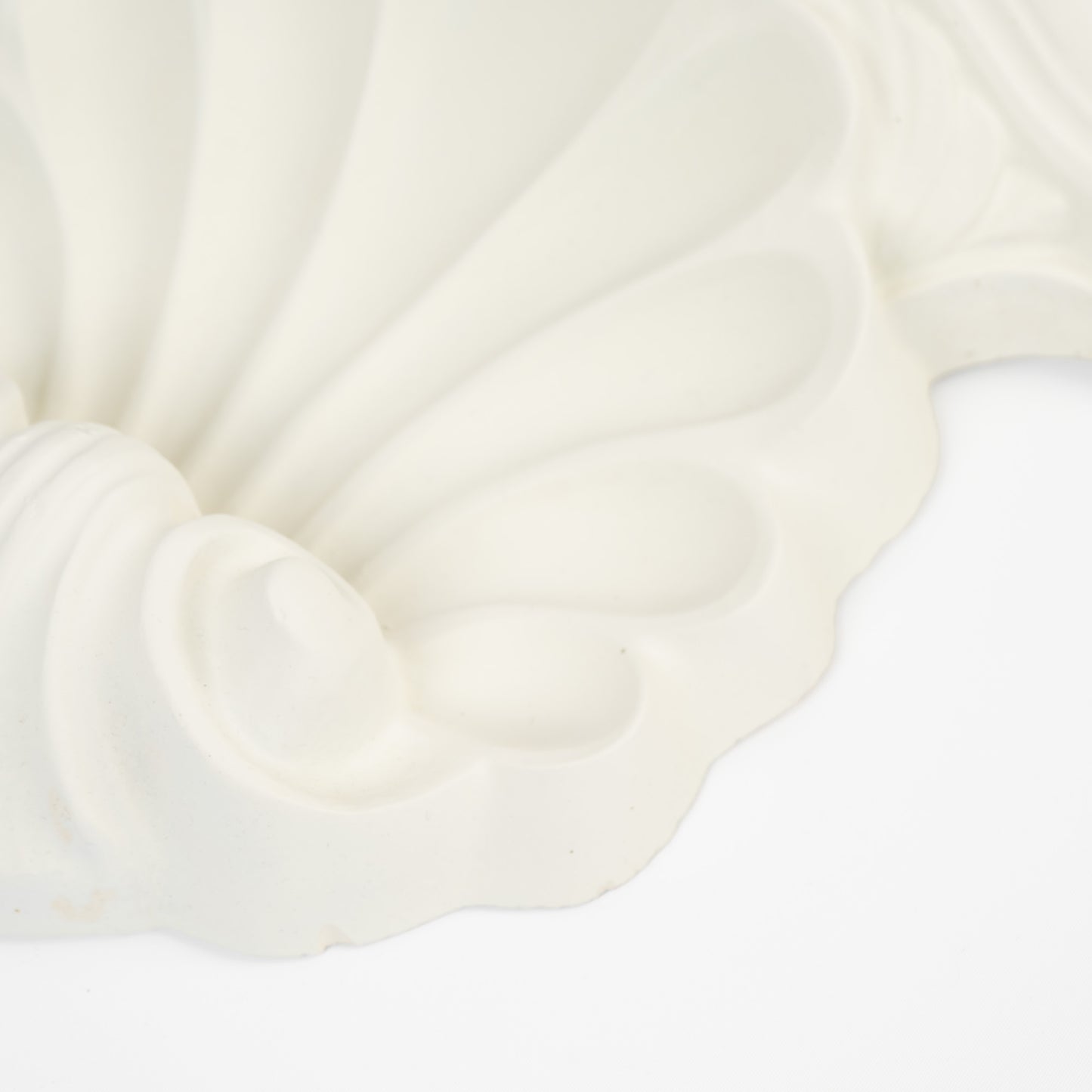Close-up of a vintage white plaster wall shelf with ornate shell and scroll corbel detailing