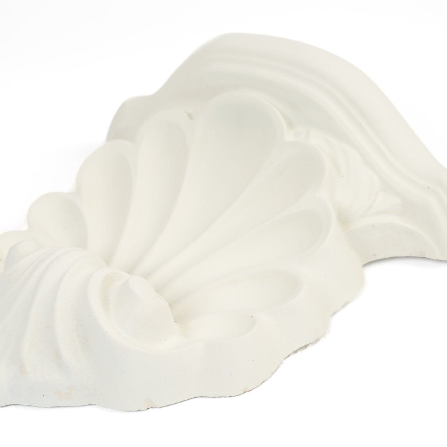 Close-up of a vintage white plaster wall shelf with ornate shell and scroll corbel detailing