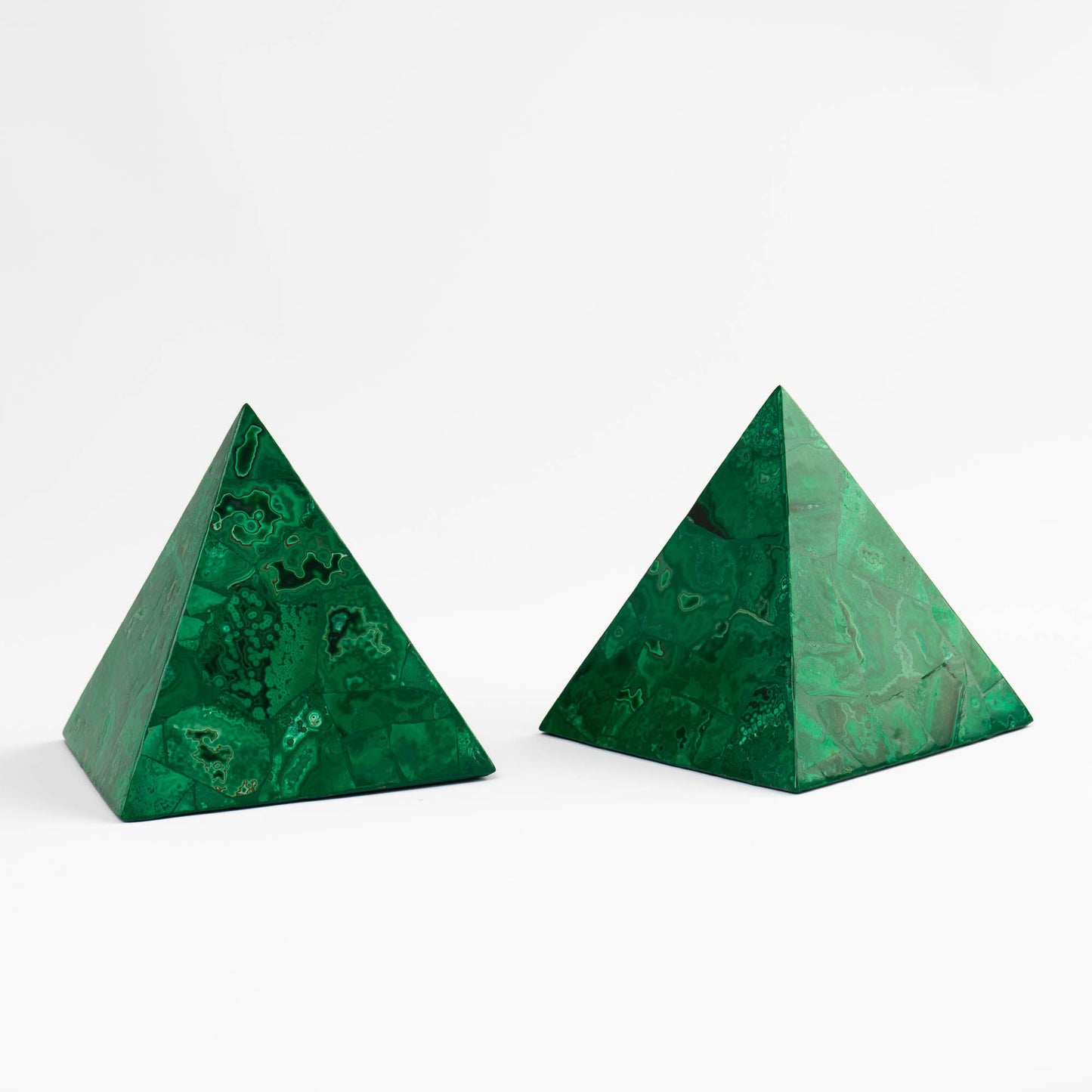 Side view of a pair of polished green malachite pyramid sculptures with natural banded stone pattern.