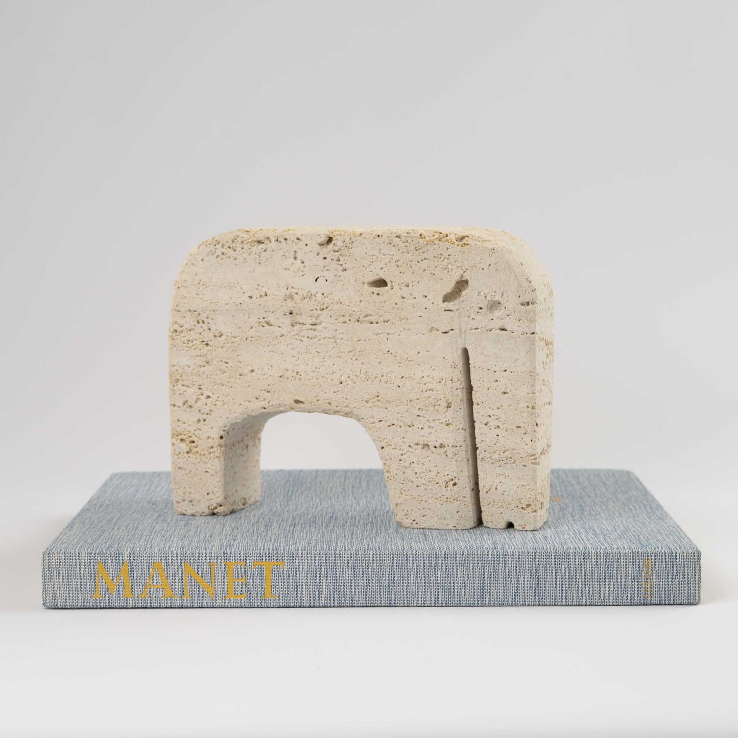 Vintage brutalist travertine elephant sculpture in warm beige stone, showing geometric angular carved details, attributed to Enzo Mari for Fratelli Manelli