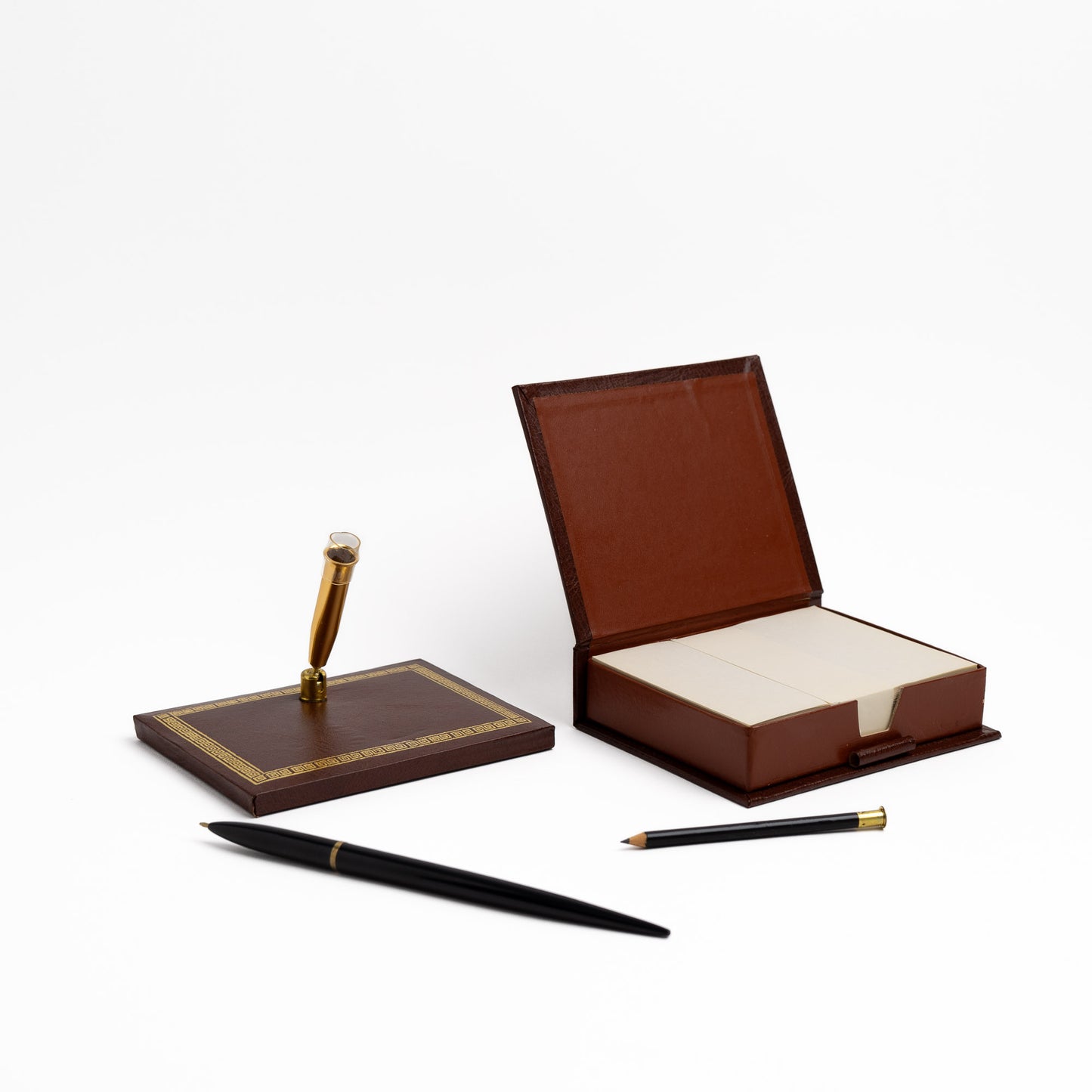 A dark brown leather desk set featuring a pen stand with a black pen and a matching closed note card box, both decorated with gold Greek key trim.