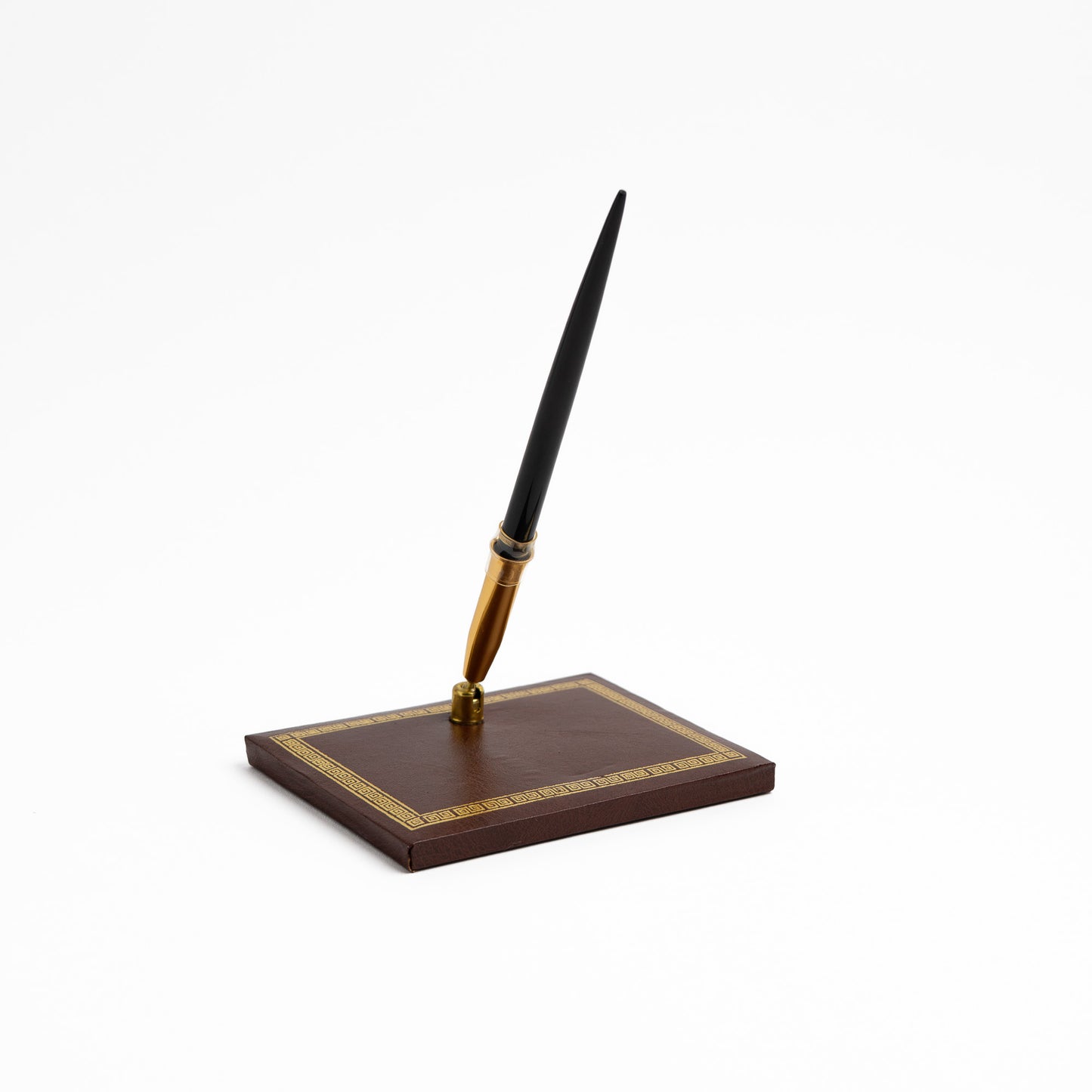A black and gold pen standing upright on a dark brown leather pen holder. with gold Greek key border detailing
