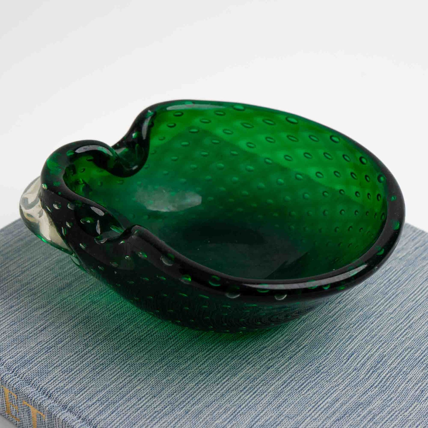 Vintage emerald green Murano glass bullicante catchall dish with controlled bubble pattern, styled on top of a vintage blue book