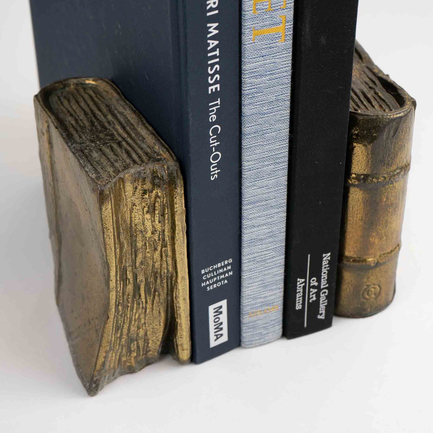 Pair of vintage brass bookends shaped like books, shown holding books on shelf