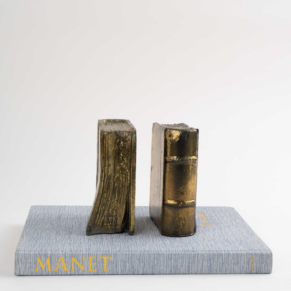 
                  
                    Pair of vintage brass bookends shaped like books, shown holding books on shelf
                  
                