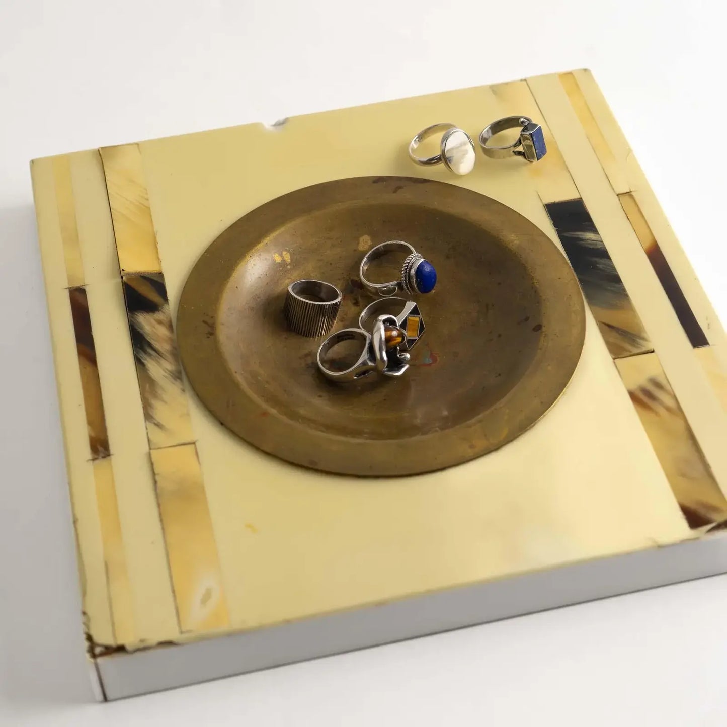 A set of vintage silver rings with various colorful stones and textured bands, displayed on a square horn and brass catchall